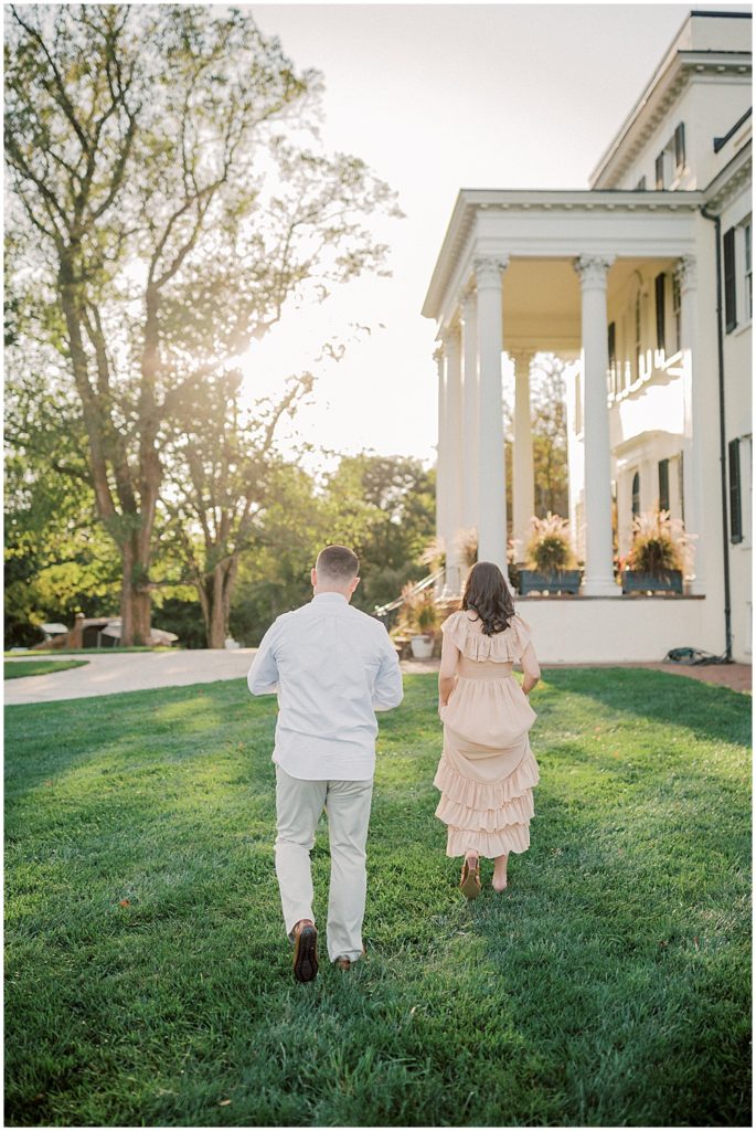 New Parents Walk Towards Oatlands Historic Home During Newborn Session By Loudoun County Newborn Photographer Marie Elizabeth Photography.