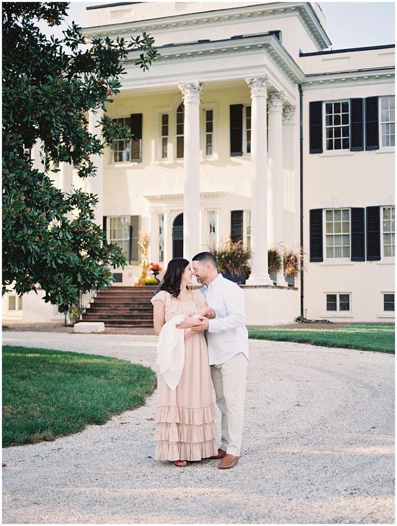 Father And Mother Hold Infant Son While Standing In Front Of Oatlands Historic Home During Newborn Session By Loudoun County Newborn Photographer Marie Elizabeth Photography.