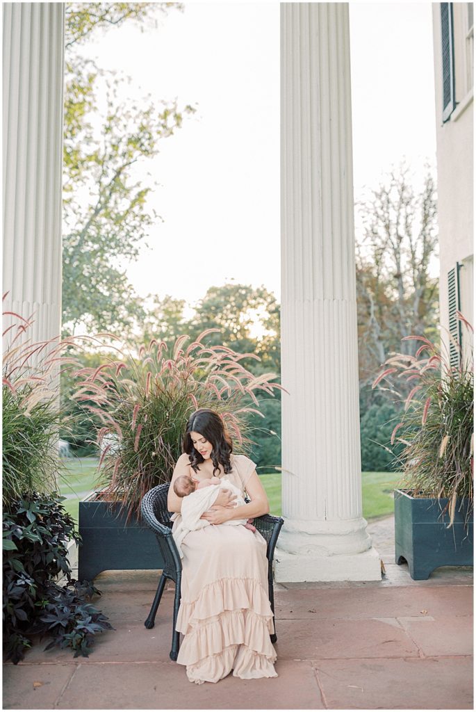 Mother Sits On Porch Of Oatlands Historic Home, Nursing Baby During Newborn Session By Loudoun County Newborn Photographer Marie Elizabeth Photography.