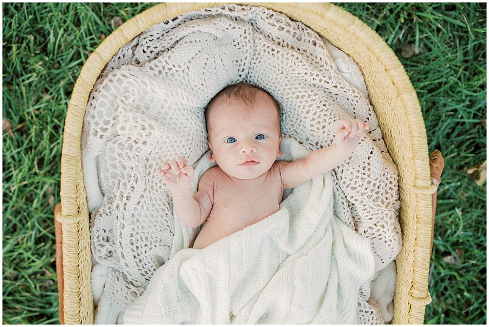 Baby Boy Lays In Moses Basket In Grass During Newborn Session By Loudoun County Newborn Photographer Marie Elizabeth Photography.