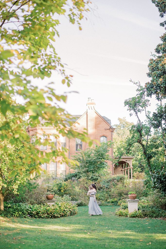 Mother Walks Across Garden Holding Son During Dc Family Session At Tudor Place.