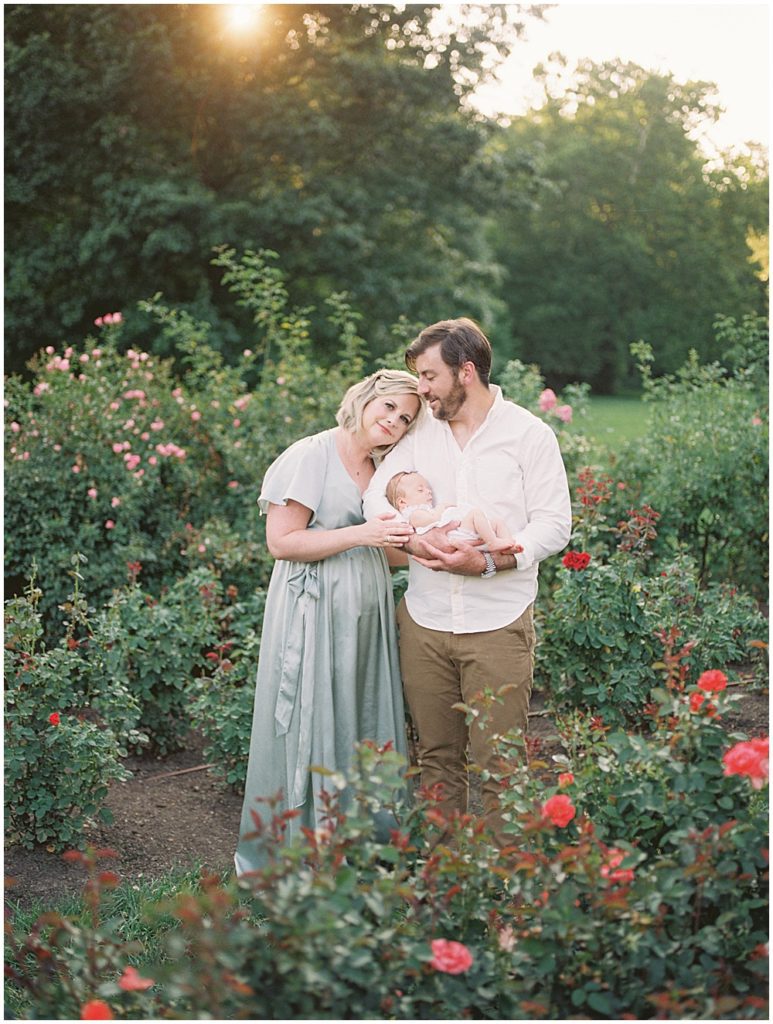 Mother Rests Her Head On Her Husband's Shoulder As They Hold Their Newborn Baby Girl.