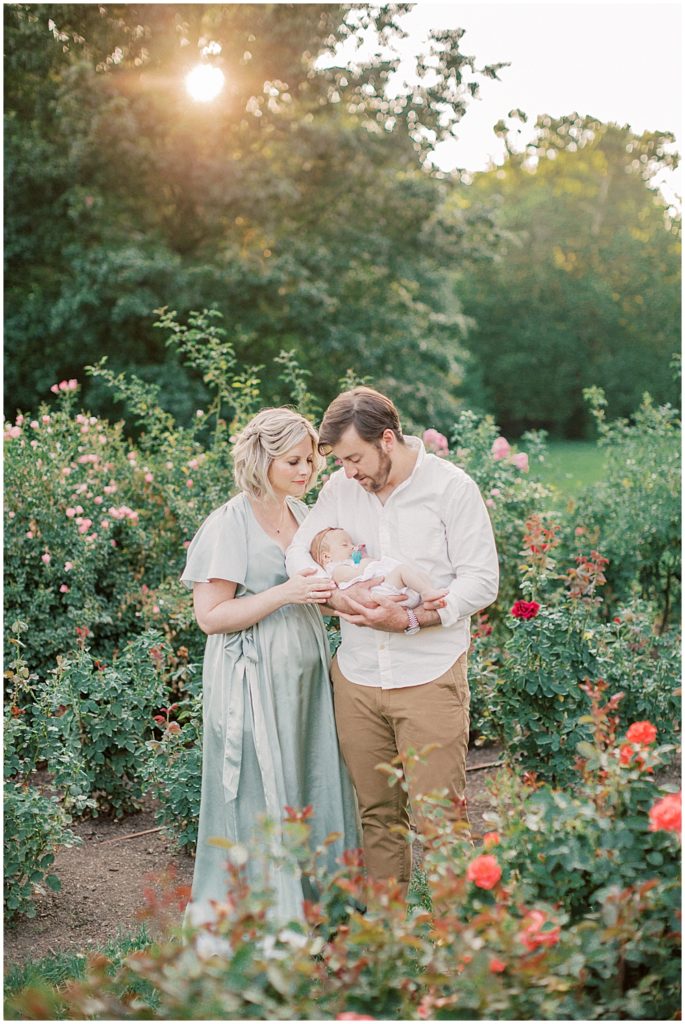 Mother And Father Hold Newborn Baby Girl During Outdoor Newborn Family Photos At Bon Air Rose Garden.