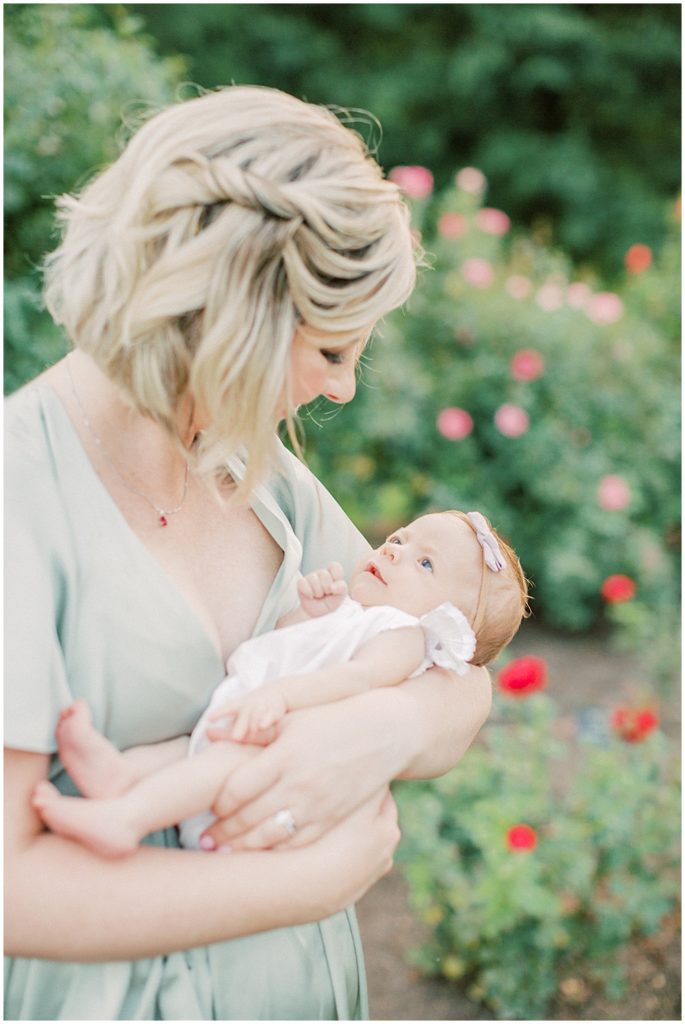 Mother Smiles Down While Holding Her  Newborn Baby Girl During Outdoor Newborn Family Photos At Bon Air Rose Garden.