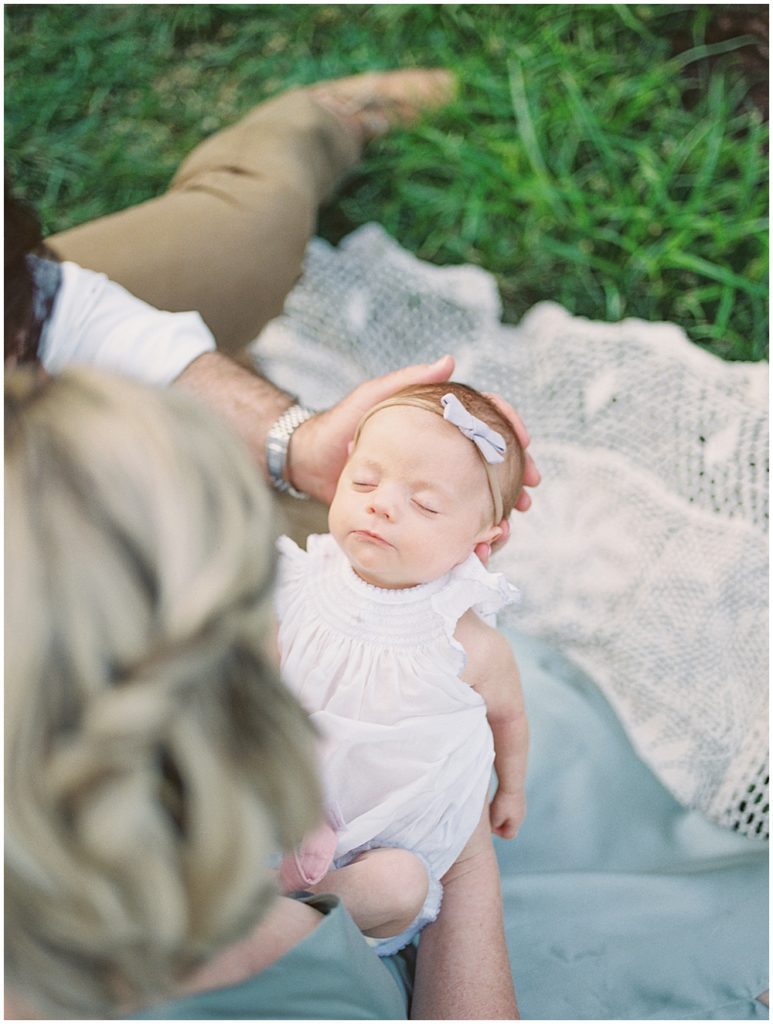 Newborn Baby Girl Sleeps As She Is Held By Her Parents During Outdoor Newborn Family Photos At Bon Air Rose Garden.