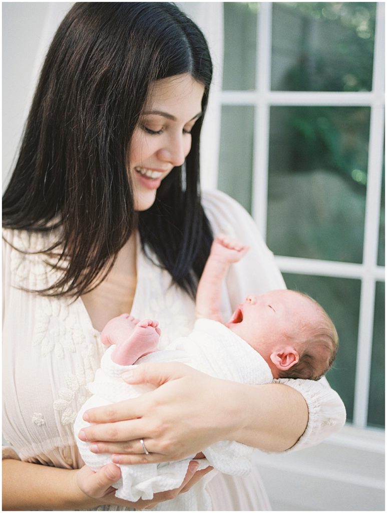 Newborn Baby Boy Held By His Mother Stretches His Arm During Studio Newborn Session.