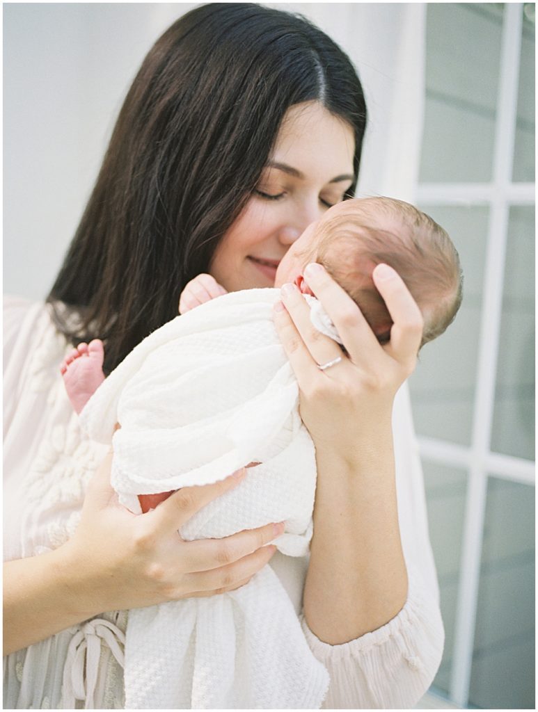 Mother Closes Her Eyes And Brings Baby Up To Her Face During Studio Newborn Session.