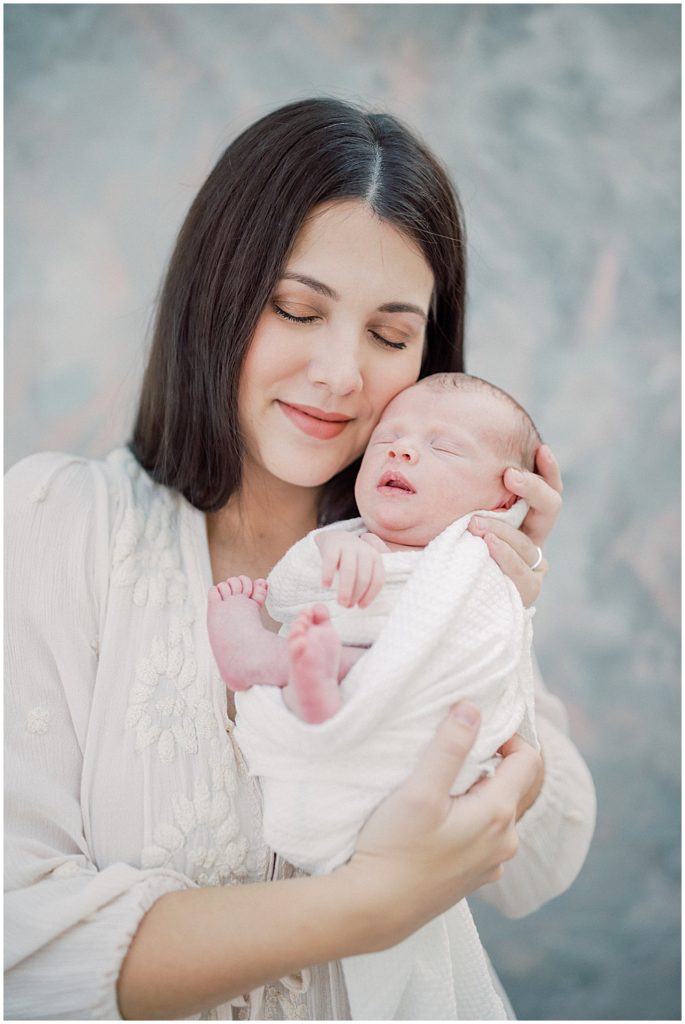 Mother Holds Newborn Baby Up To Face And Closes Her Eyes During Studio Newborn Session.