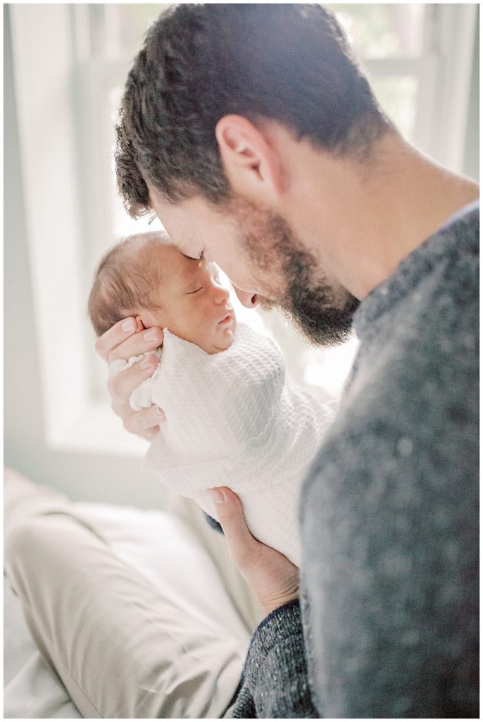 Father In Gray Sweater Brings Baby Boy Up To His Face During Dc Row House Newborn Session.