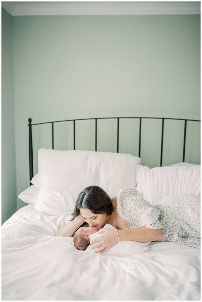 Mother Lays On Bed With Baby Boy, Kissing His Face During Dc Row House Newborn Session.