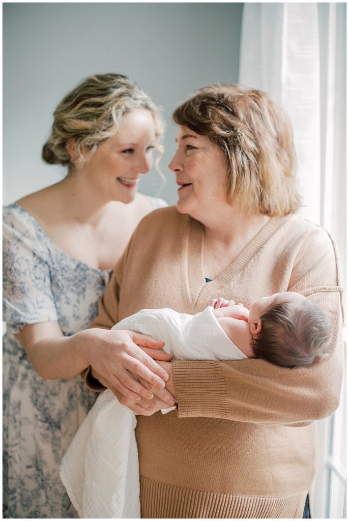 Mother And Grandmother Hold Newborn Girl And Smile At Each Other During Fairfax Va Newborn Session.