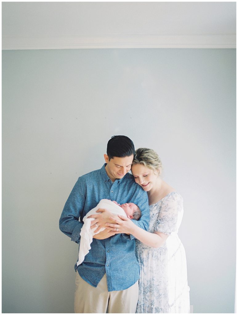 Mother And Father Lean In Close To Each Other While Smiling At Their Baby Girl.