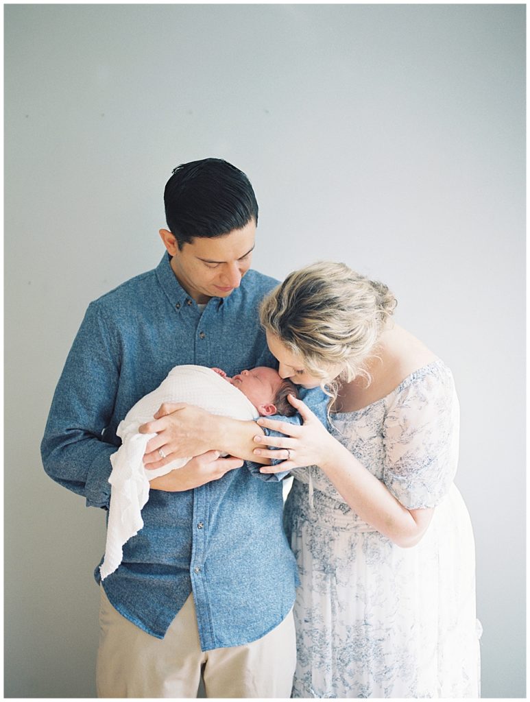 Mother With Blonde Hair Leans In To Kiss Her Newborn Baby During Fairfax Va Newborn Session.