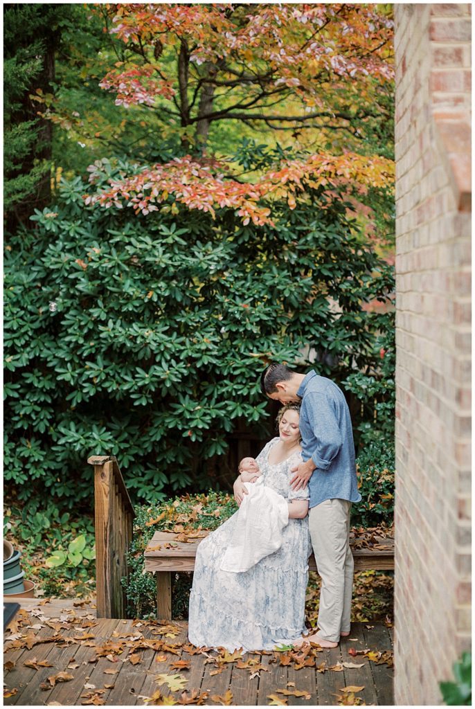 Mother Sits On Bench Outside In Front Of Fall Foliage During Fairfax Va Newborn Session.