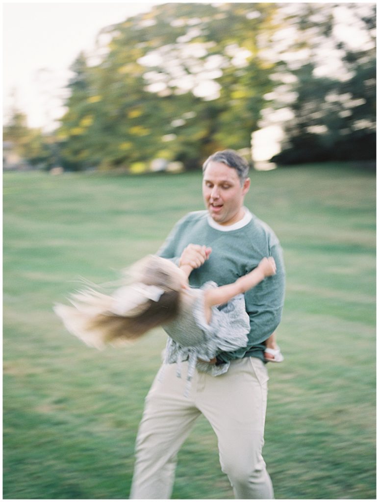 Father In Green Sweater Spins His Toddler Daughter In Circles During Glenview Mansion Photos By Marie Elizabeth Photography.