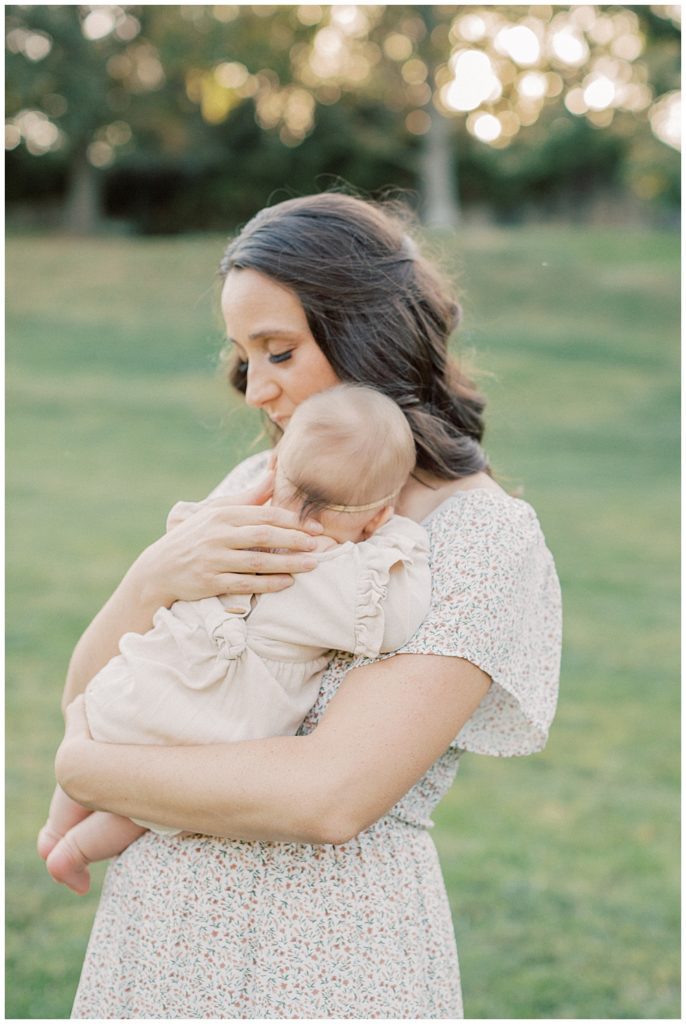 Mother Comforts Infant Daughter While Standing In A Field During Glenview Mansion Photos By Marie Elizabeth Photography.