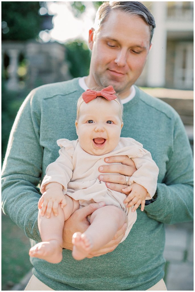 Father Holds His Baby Girl With Red Bow As She Smiles.