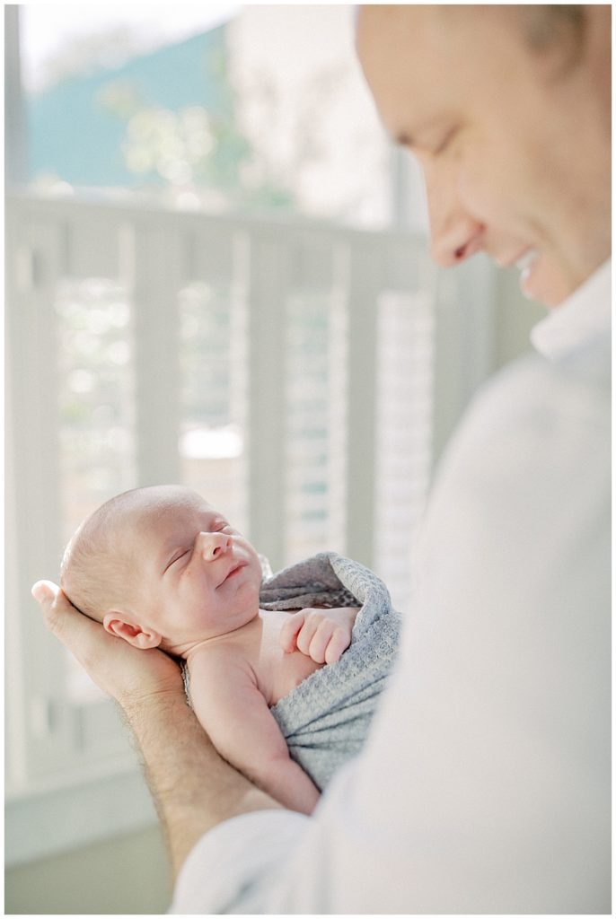 Newborn Baby Boy Smiles While Being Held By His Father.