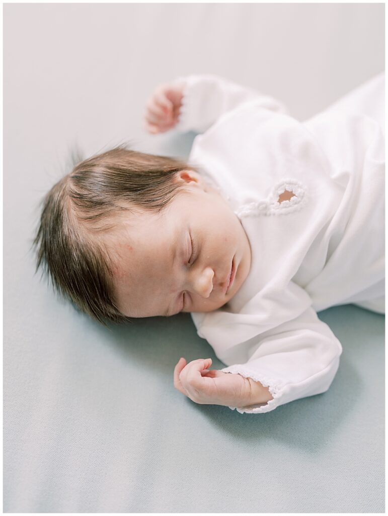 Baby Girl In White Outfit Sleeps On A Blue Blanket.