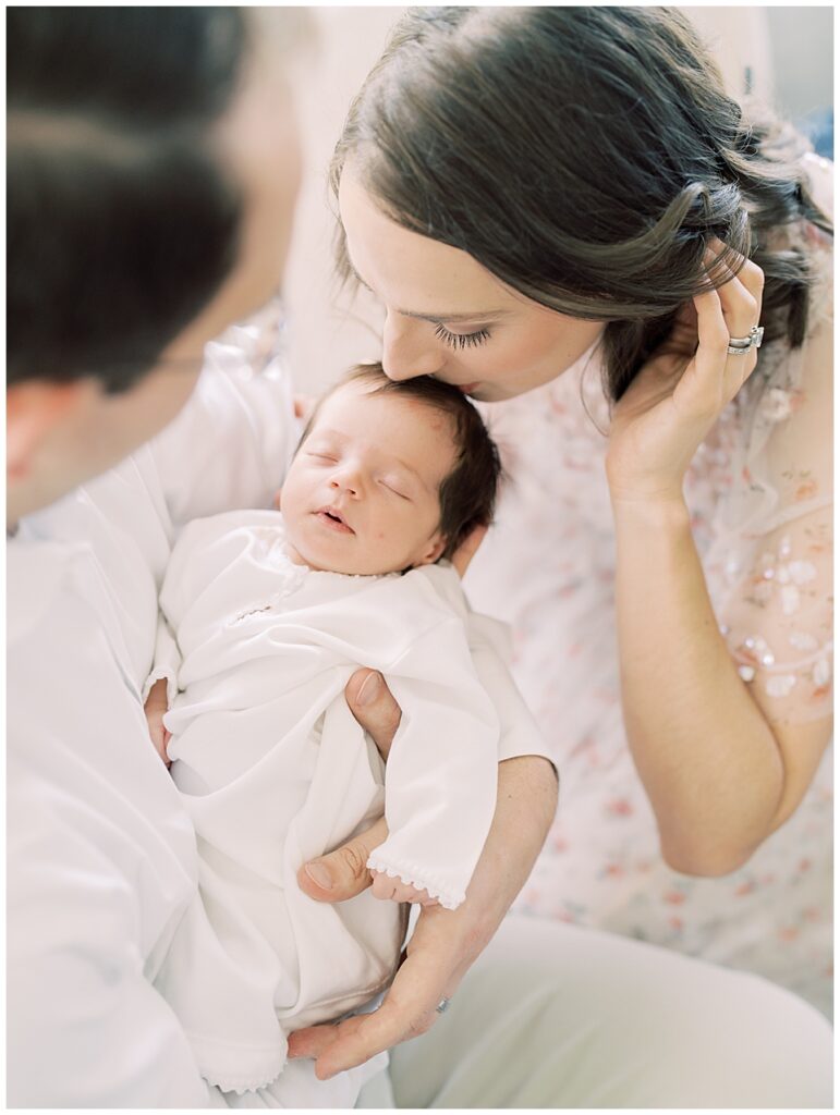 Mother With Brown Hair Leans Down And Kisses The Top Of Her Baby's Head While Her Husband Holds Baby Photographed By Arlington Newborn Photographer Marie Elizabeth Photography.