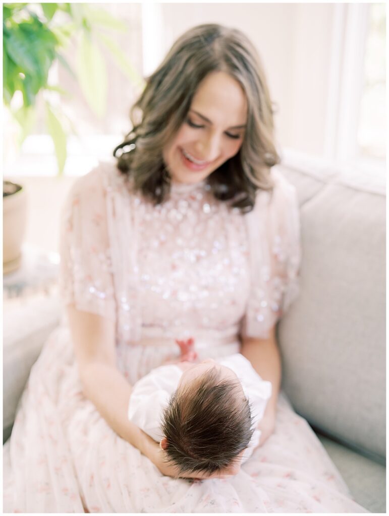 Mother Smiles Down At Her Baby Girl As She Holds Her In Her Lap In Her Home.