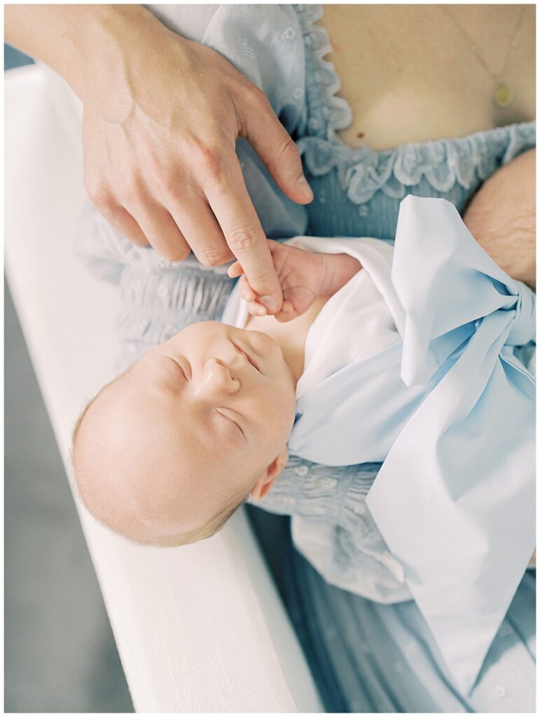 Close-Up View Of Dad Reaching Finger Out To Baby As Baby Wraps Fingers Around Dad's While Wearing Beaufort Bonnet Swaddle.