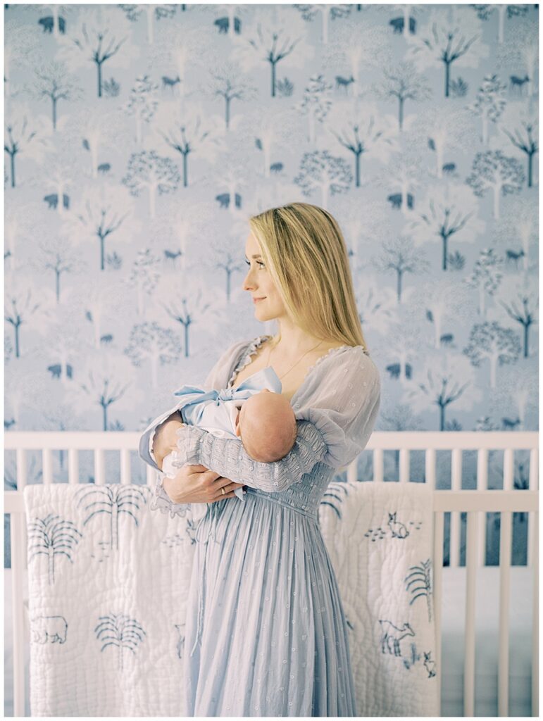 A Mother In A Blue Doen Dress Stand Holding Her Baby Boy In Her Serena &Amp; Lily Nursery, Photographed By Newborn Photographer Marie Elizabeth Photography.