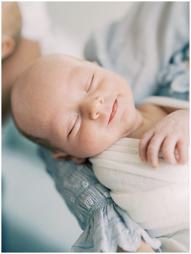 A Close-Up Of A Baby Boy Held By His Mother In A Blue Dress Smiling, Photographed By Chevy Chase Newborn Photographer Marie Elizabeth Photography.