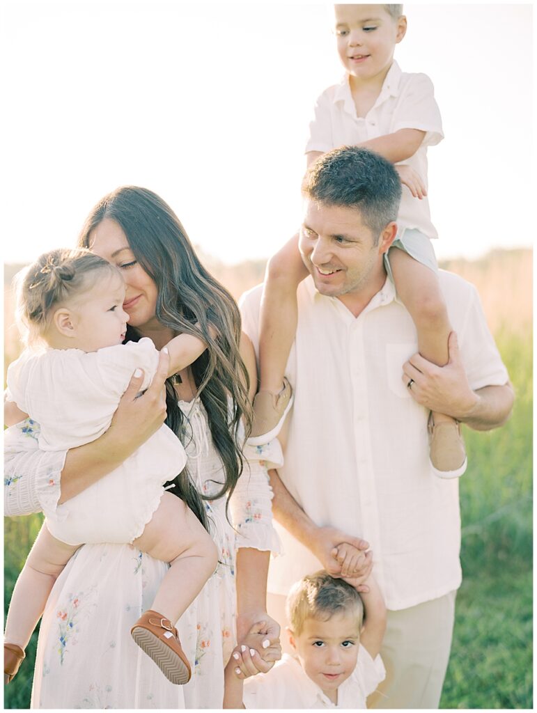 Mother And Father Stand With Their Three Young Children Holding Them And Smiling During Manassas Battlefield Family Session.