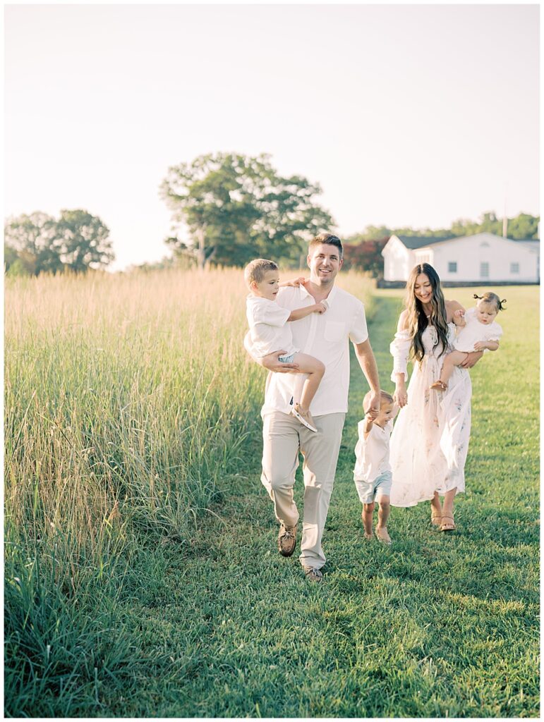 Father Holds Hands With His Family And Leads Them Down A Path Along A Field During Manassas Battlefield Family Session.