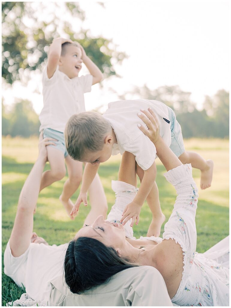 Mother Holds Up Little Boy In The Air While Laying On Her Husband's Lap As He Holds Up Different Little Boy.