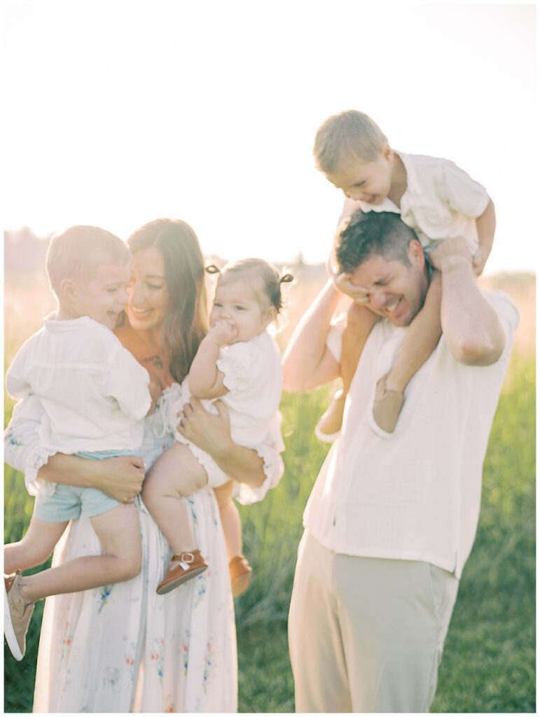 Mother And Father Laugh And Hold Three Young Children At Sunrise During Manassas Battlefield Family Session.