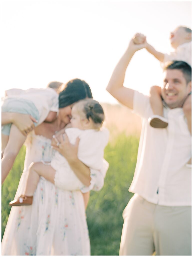 Out-Of-Focus Image Of Mother And Father With Three Young Children Smiling.