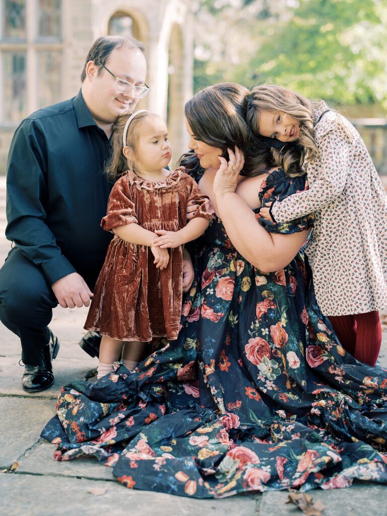 Mother dresses in black floral Selkie dress kneels down to her two daughters and husband during a Virginia House family session in Richmond, VA.