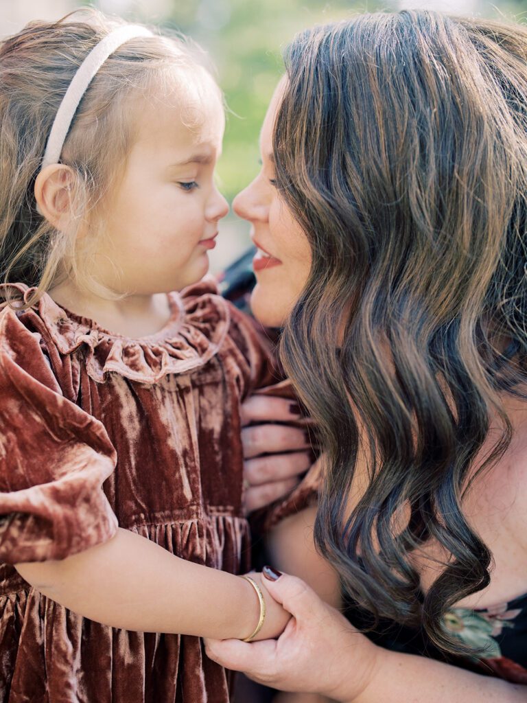 Close-up view of mother with long brown hair giving a nose nuzzle to her young daughter.