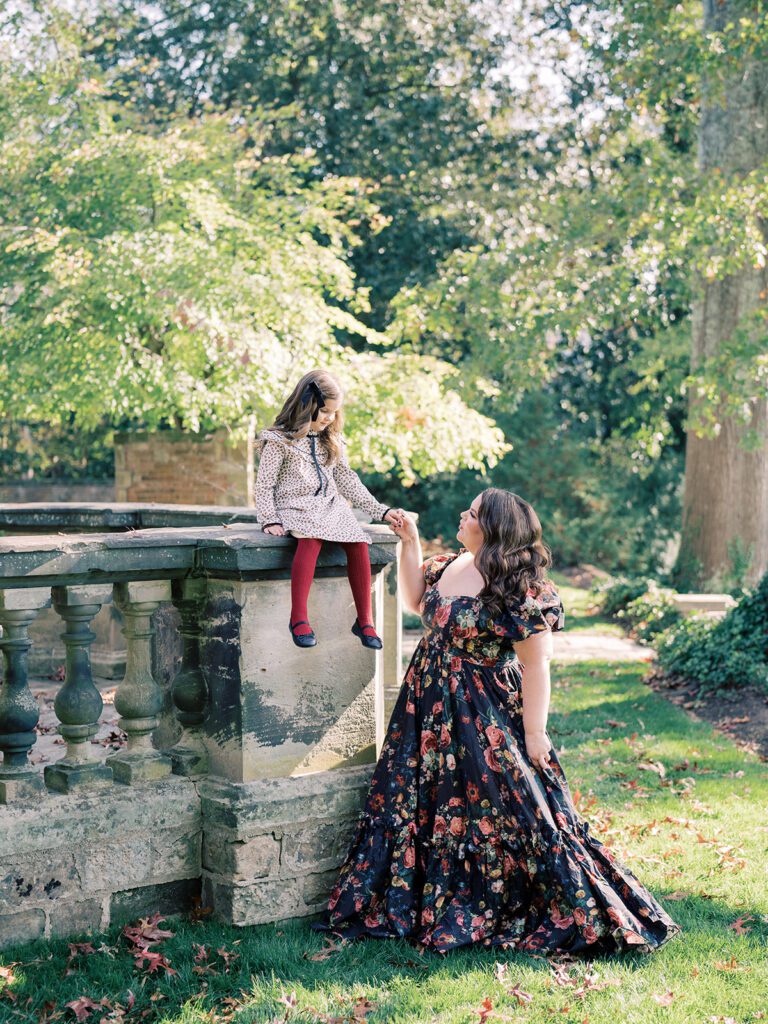 Mother in black floral Selkie dress looks up and holds the hand of her daughter sitting on a balcony at the Virginia House.