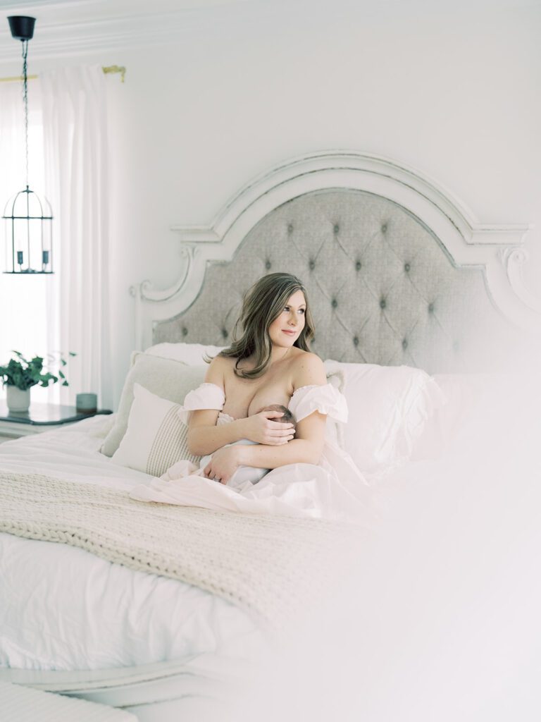 Mother Sits On Bed, Nursing Baby While Looking Out The Window.