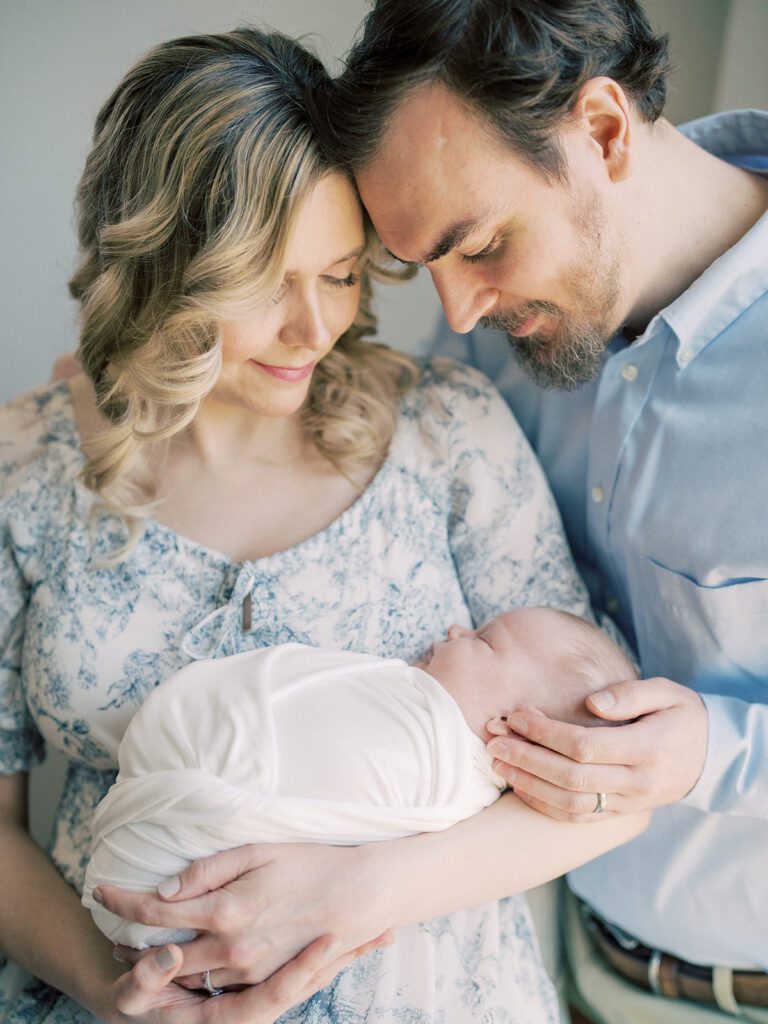 Father And Mother Lean In Close And Smile At Their Baby.