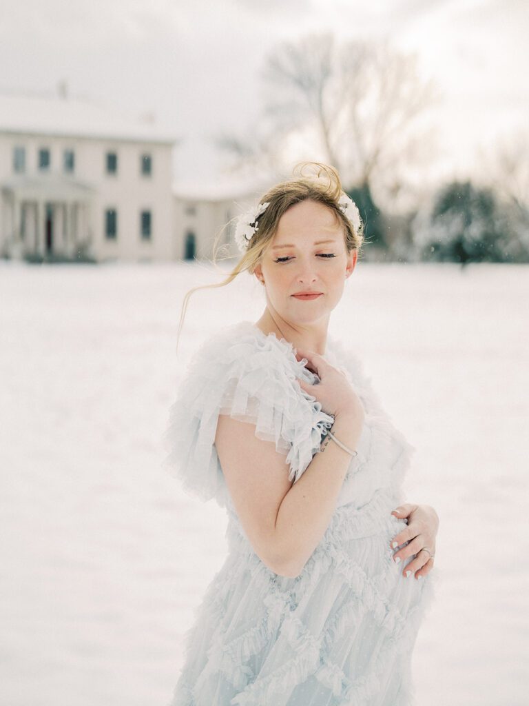 A Winter Maternity Session In The Snow With A Mother With Red Hair In A White Floral Crown And Light Blue Needle &Amp; Thread Dress.