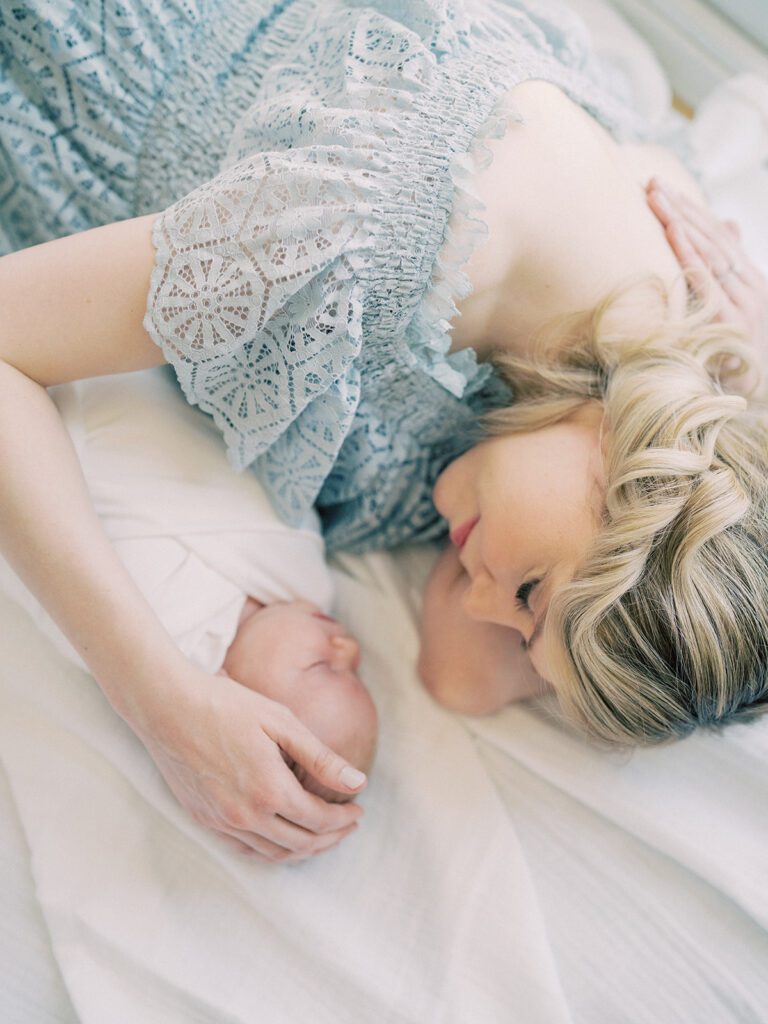 Blonde Mother In Light Blue Dress Lays Down On A White Blanket With Her Newborn Baby During Her Silver Spring Md Newborn Session.