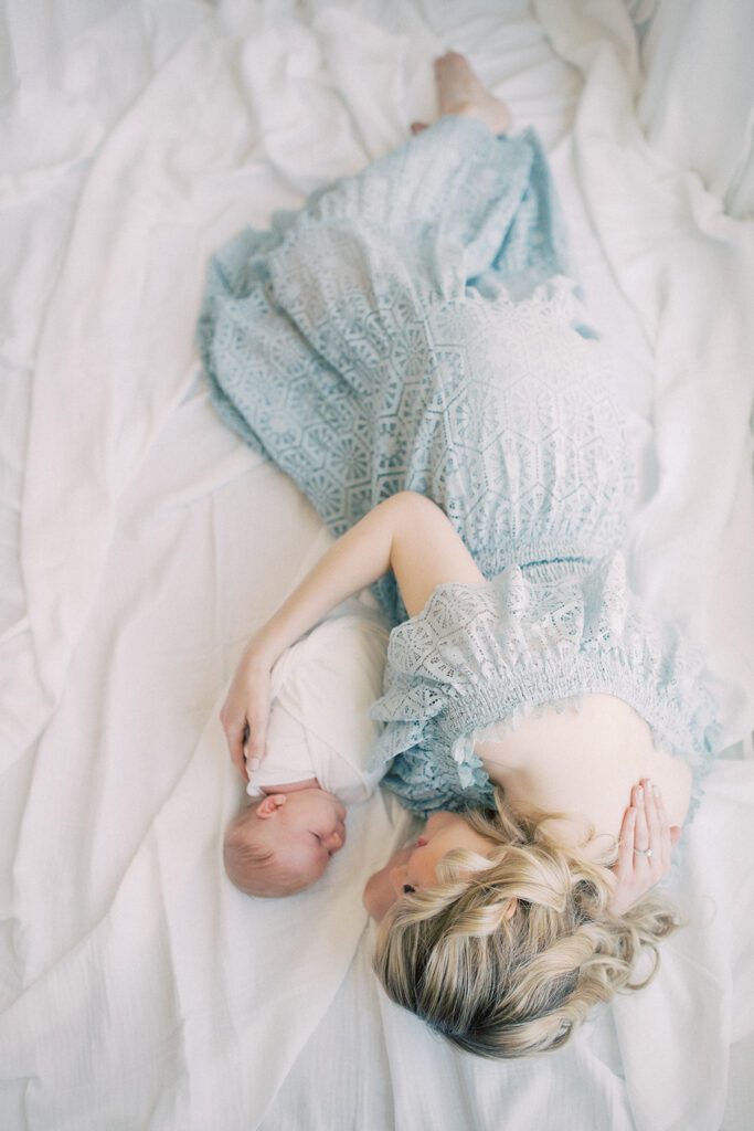 Blonde Mother Lays Down On White Blanket With Arm Wrapped Around Her Newborn Baby During Her Silver Spring Md Newborn Session.