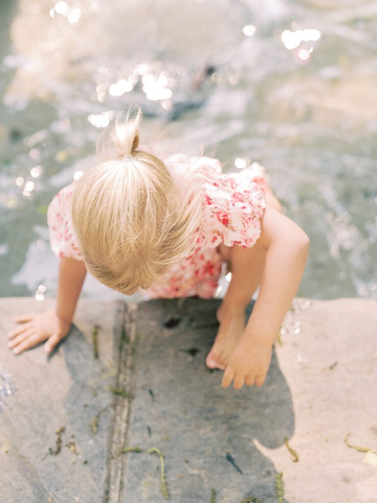 Little blonde girl in pink floral dress steps out of a fountain at Glenview Mansion MD.