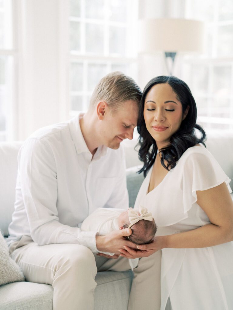 A Father Leans Into His Wife As They Hold Their Newborn Baby.