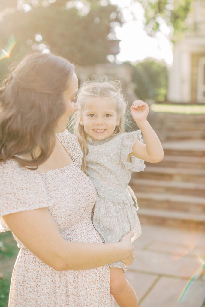 Little girl smiles as her mother holds her.