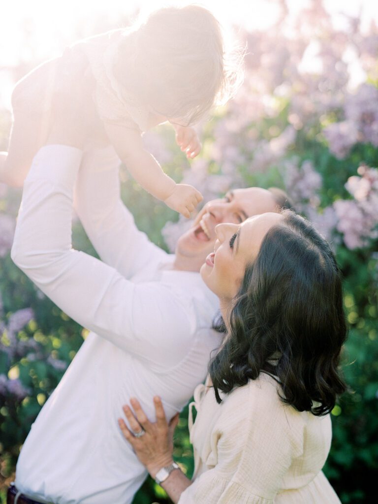 Little girl is held up in the air with the sun behind her in a lilac field.