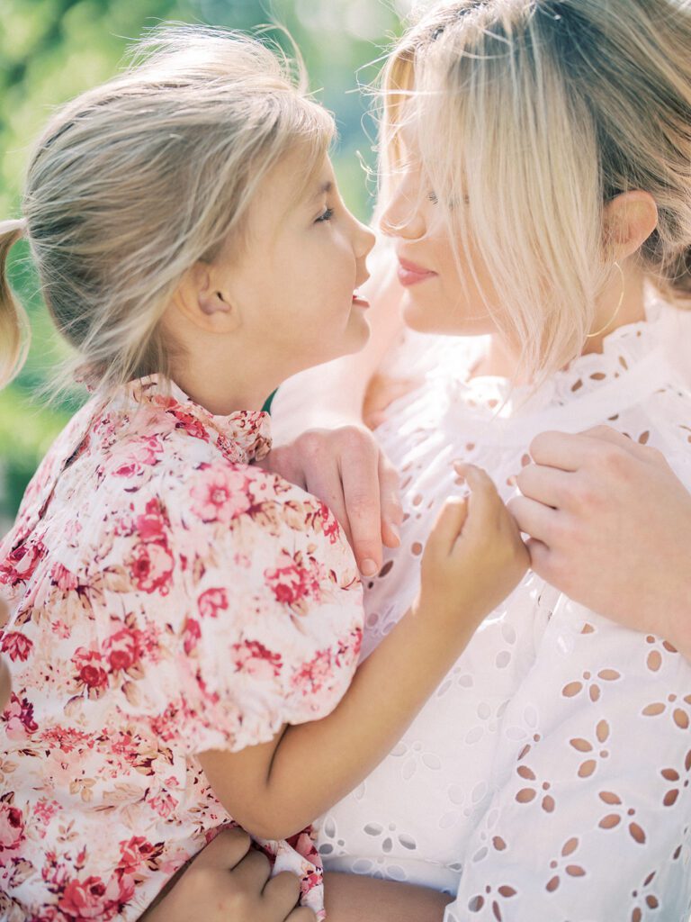 Blonde mother goes nose-to-nose with her blonde daughter during their family photo session.