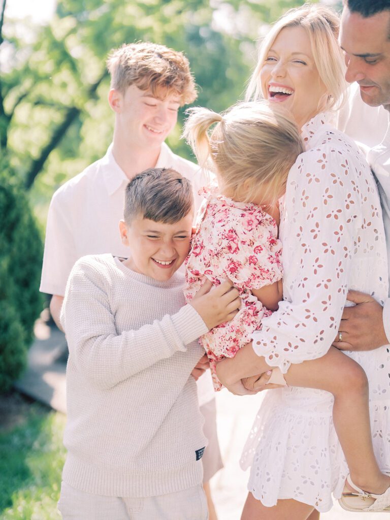 Mother laughs while holding her daughter and standing with her family.