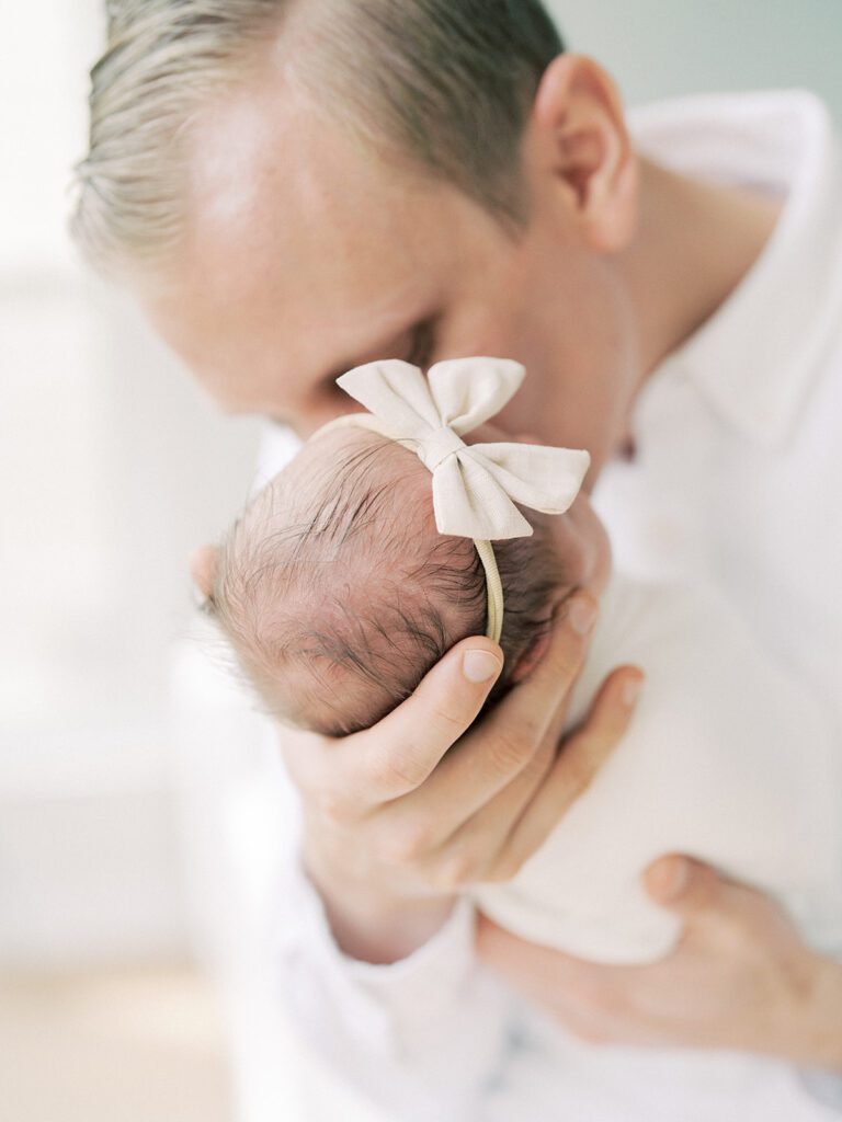 A Father With Blonde Hair Brings His Newborn Baby Up For A Kiss.