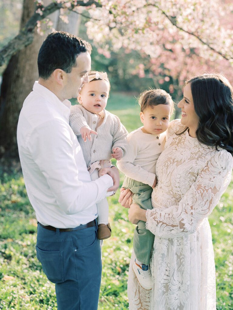 Mother And Father Smile At Each Other While Holding Their Two Small Children.