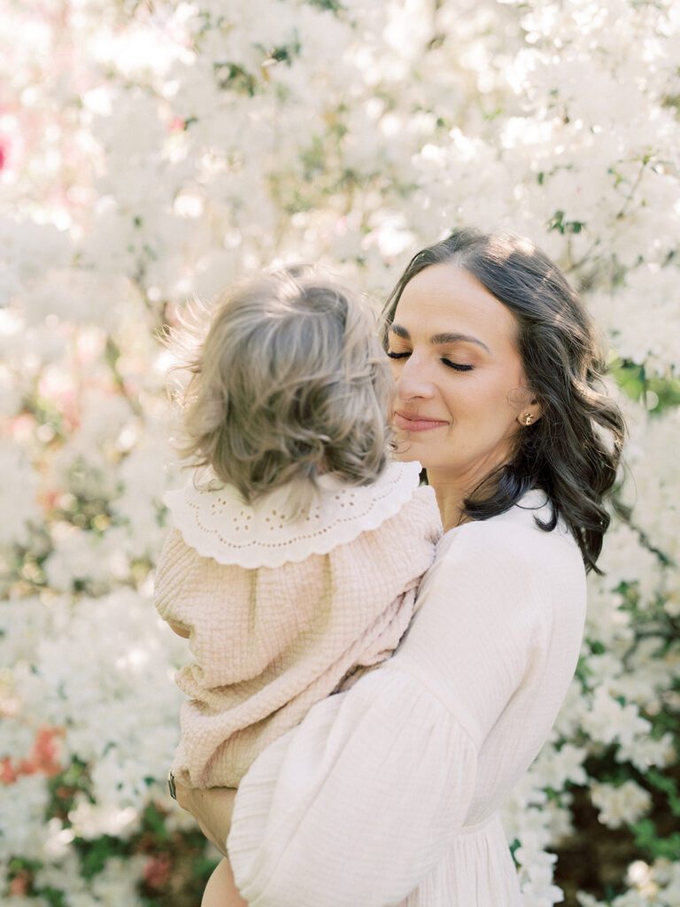 Mother Holds Her Toddler Daughter In Front Of A White Azalea Bush At The National Arboretum.